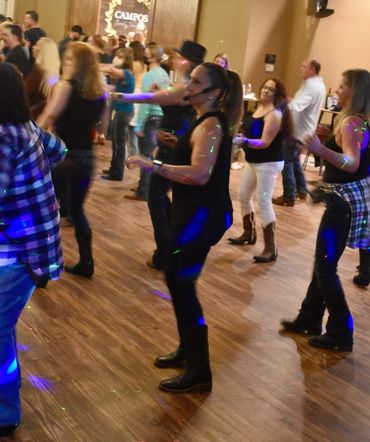 Group of people line dancing in a lively indoor setting with colorful lights.