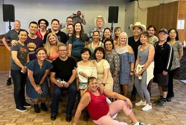A large group of diverse adults smiling and posing indoors on a wooden floor.