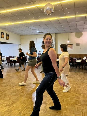 Women dancing together joyfully in a community hall with a disco ball.