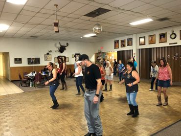A group of people line dancing indoors in a community hall.