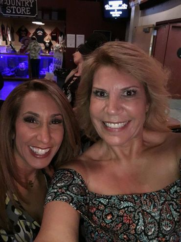 Two women smiling and taking a selfie at a lively country store bar.