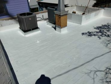 Newly coated white flat roof with HVAC units and chimney.