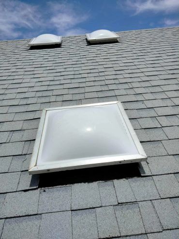 Three skylights on a gray shingled roof under a partly cloudy sky.