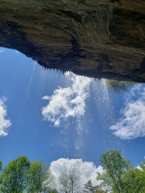 Waterfall droplets falling from a rocky cliff against a blue sky.