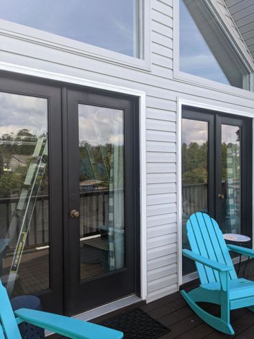 Blue rocking chairs on a wooden deck outside black-framed glass doors.