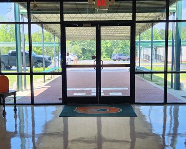 View through large glass doors to a covered walkway and parked vehicles outside.