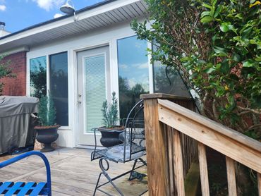 Cozy backyard patio with seating, plants, and a grill under blue sky.