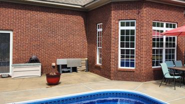 Backyard pool area with brick walls, patio furniture, and sun umbrella.