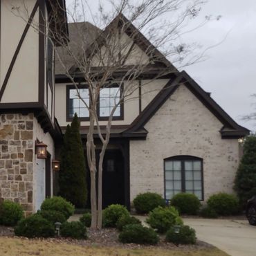 A charming Tudor-style house with stone and brick exterior and manicured bushes.