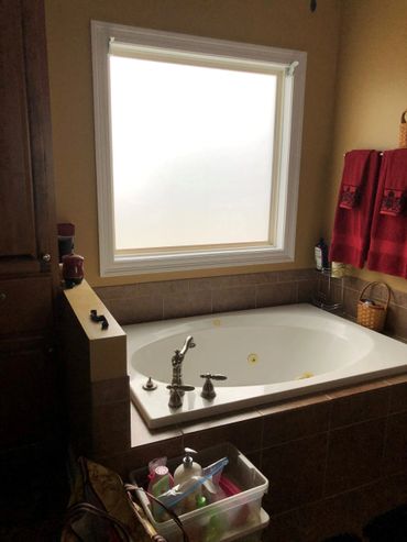 Bathtub with frosted window and red towels in cozy bathroom.