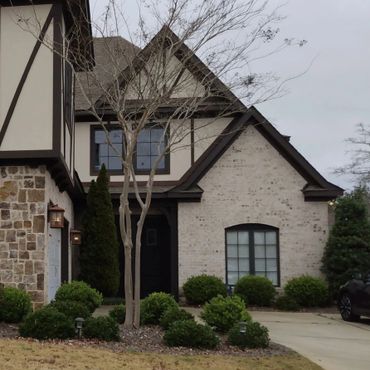 A Tudor-style house with stone and brick exterior and manicured bushes.