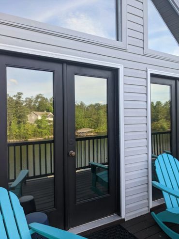 Reflection of a lake and trees on glass doors with blue chairs nearby.