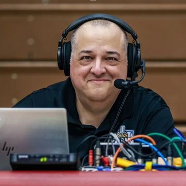 Man wearing headset sitting behind audio equipment and laptop.