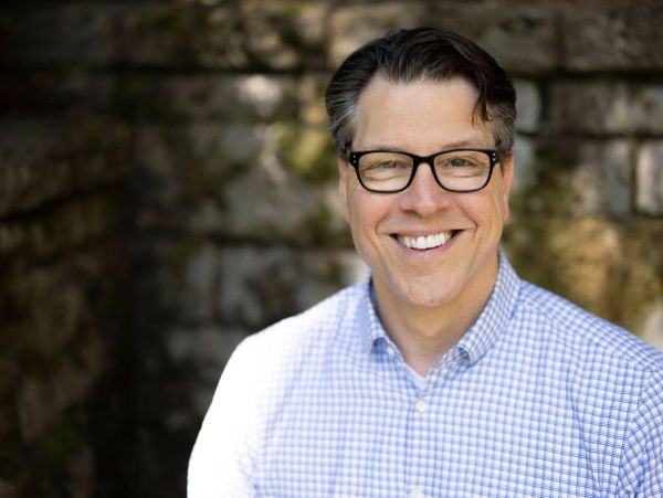 Smiling man with glasses in a checkered shirt outdoors.