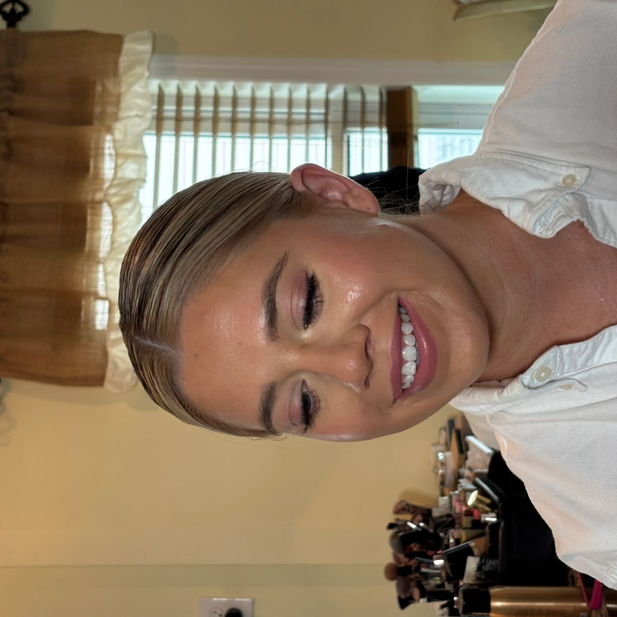 Smiling woman with makeup and hair tied back, wearing a white buttoned shirt.