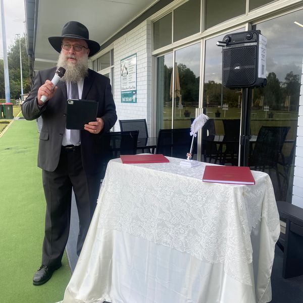 Man in suit and hat speaking at a covered outdoor event.