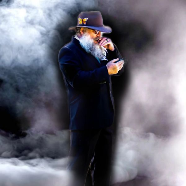 Man in dark suit with butterfly on hat in misty setting.