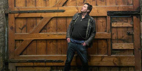 Man leaning against a large wooden door, looking upwards.