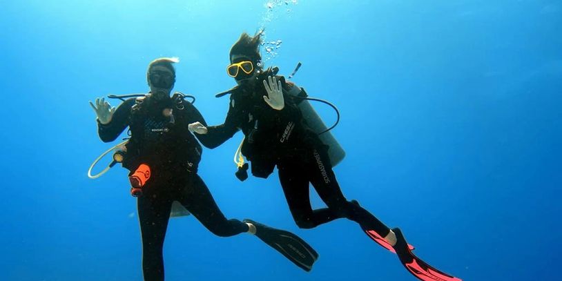 Two scuba divers underwater waving with clear blue ocean around.