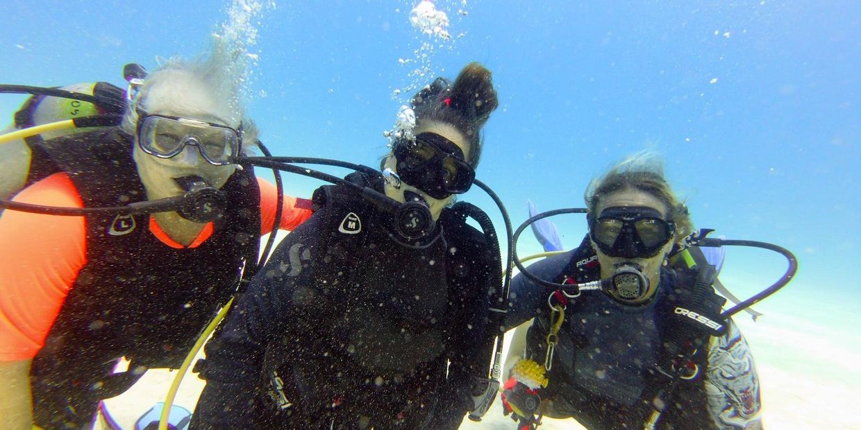 Three scuba divers posing underwater with gear and bubbles around them.