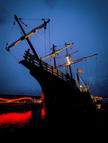 Historic ship at dusk with glowing red reflections.