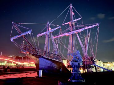 Illuminated tall ship and statue against a starry night sky. Whitehaven.