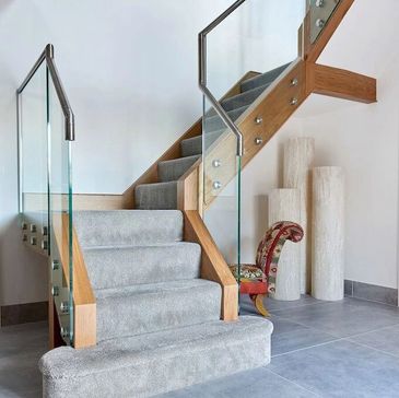 Glass stair case with wooden hand rail and grey carpet