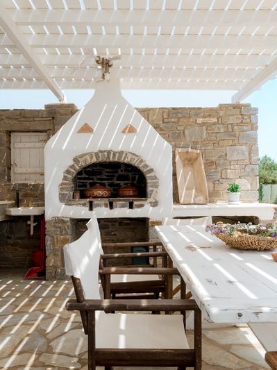 Sunlit outdoor dining area with white wooden table and chairs under a shaded pergola.