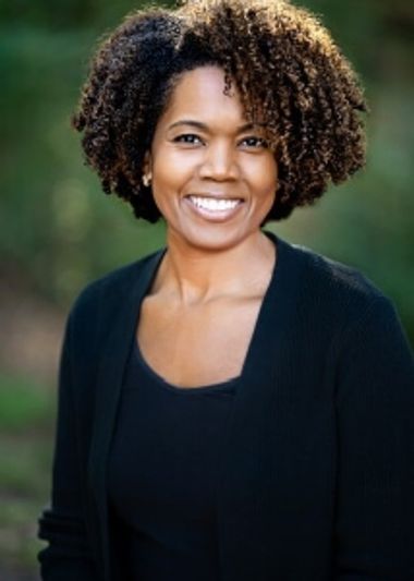 Smiling woman with curly hair in outdoor setting.