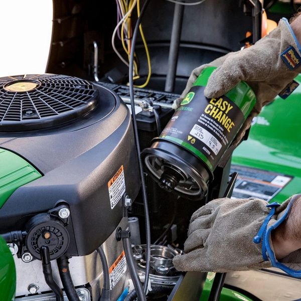 Person changing oil filter on a green John Deere engine, wearing protective gloves.