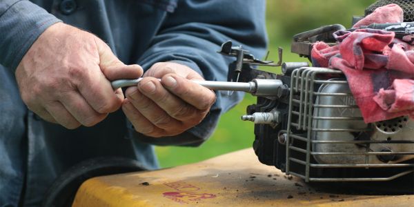 Person using a socket wrench on a small engine outdoors.