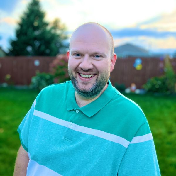Smiling man in a green and white polo shirt outdoors at sunset.