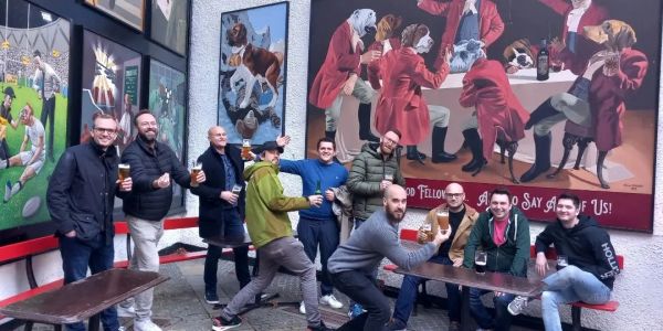 Group of men enjoying drinks in front of dog-themed murals.