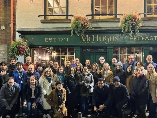 Large group posing outside McHughs pub in Belfast at night.