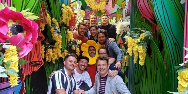 Group of men posing in colorful floral tunnel.