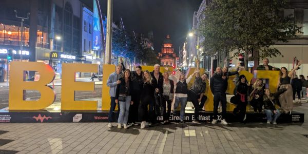 Group of people posing by large Belfast letters at night.