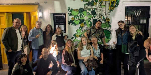 Group of people posing together outside a building with a mural.