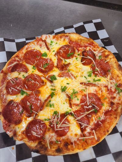 Pepperoni pizza with melted cheese and herbs on checkered paper.