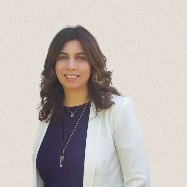 A smiling woman with wavy hair wearing a white blazer and dark top.