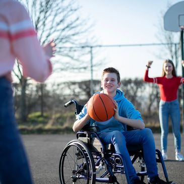 A young boy in a wheel chair playing basketball with two friends