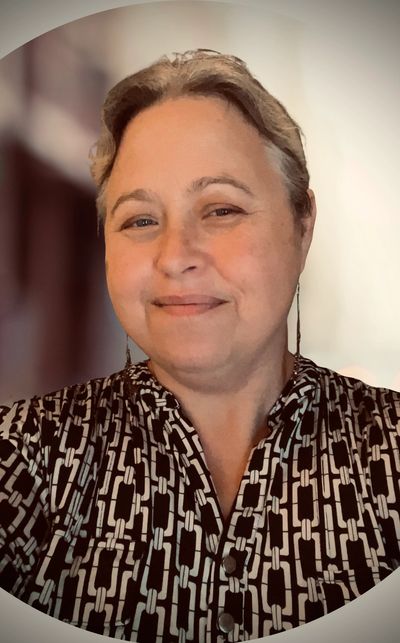 Smiling woman with short hair wearing a patterned black and white top.