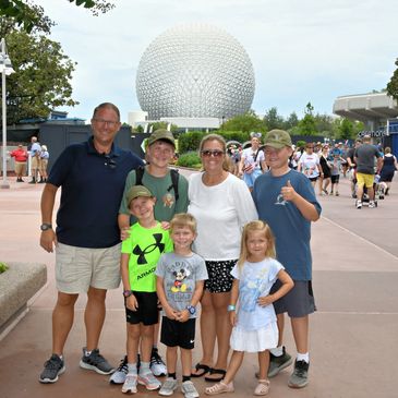 Family posing happily in front of the iconic Epcot geodesic sphere at Disney World.
