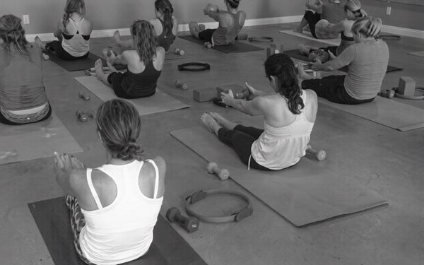 Group of women practicing yoga with light dumbbells in a studio.