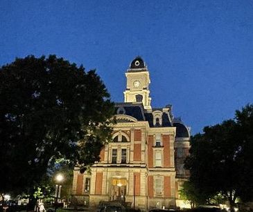 Historic building illuminated against a twilight sky with large trees