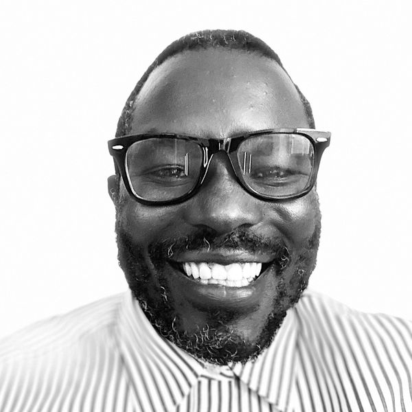 Smiling man wearing glasses and a striped shirt in black and white photo.
