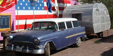 Classic Route 66 Chevy with vintage trailer and American flag display.