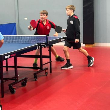 Two boys playing table tennis indoors.