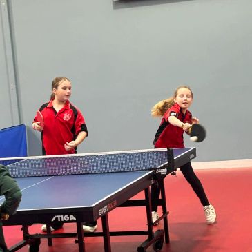 Two girls playing table tennis indoors.