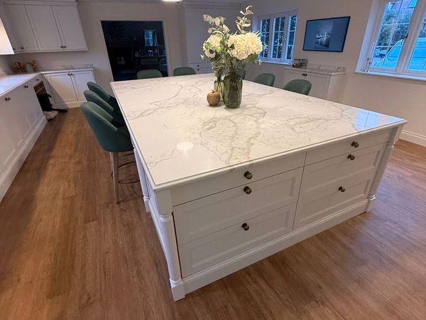 Spacious kitchen island with marble countertop and green chairs.