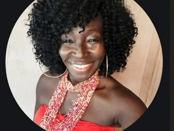 Smiling woman with curly hair and beaded necklace.